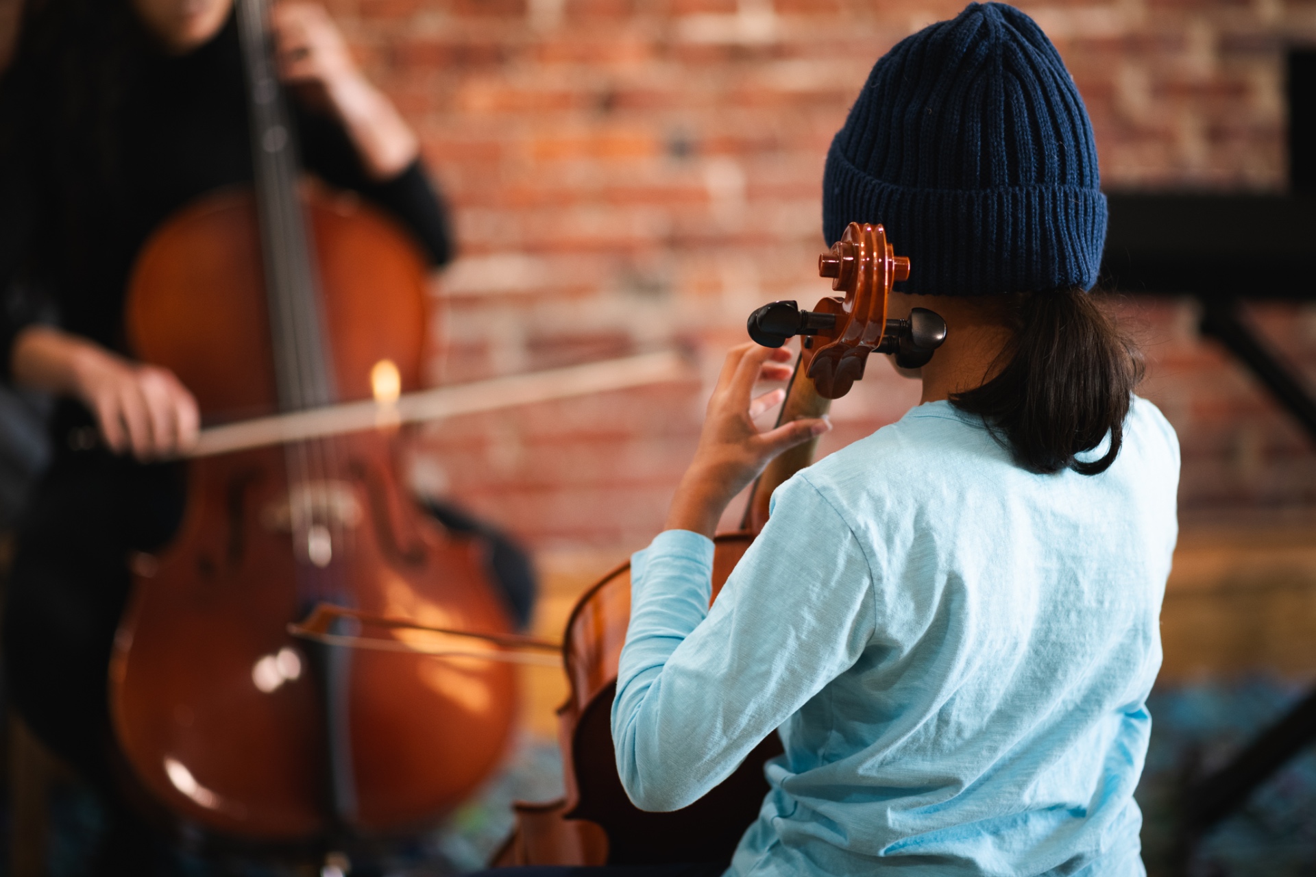 Student in a beanie playing cello alongside teacher
